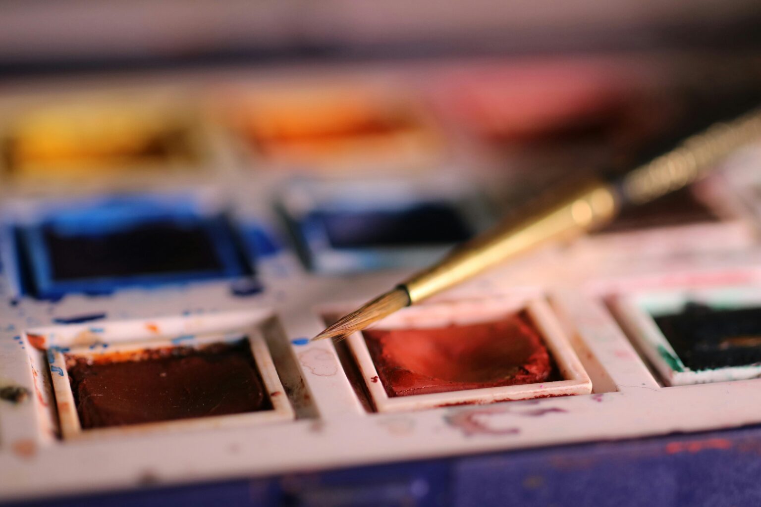 Detailed view of a watercolor palette with a brush on red paint, ideal for artistic themes.